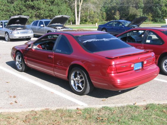 red coupe parked next to other cars, some with hoods up