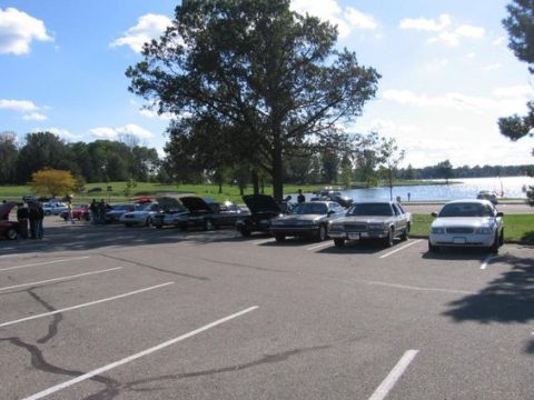 1988 Mercury Grand Marquis - Cars gathered in a parking lot near a lake on a sunny day.