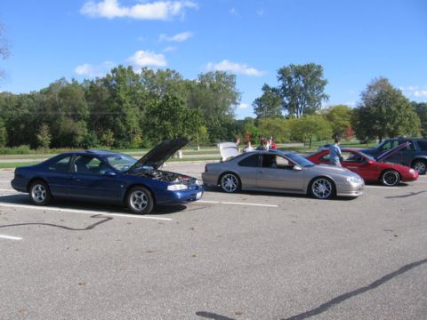 1988 Mercury Grand Marquis - Multiple coupes and an SUV are parked in a lot on a sunny day, with two of the coupes having their hoods or trunks open.