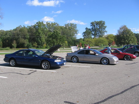 Blue coupe with hood open, silver coupe with trunk open, red coupe, and dark SUV parked in lot