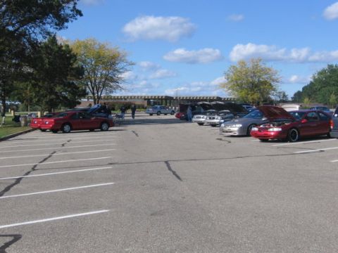 1988 Mercury Grand Marquis - A gathering of vehicles in a parking lot under a blue sky with scattered clouds.