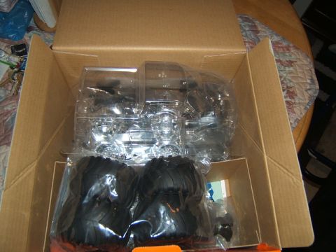 1988 Ford Bronco - RC crawler parts, including tires and a clear plastic body shell, are packed inside a cardboard box.
