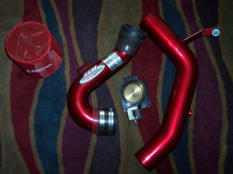 2003 Ford Focus - Red AEM cold air intake system components, including an air filter, intake tubes, and a throttle body, laid out on a striped carpet.