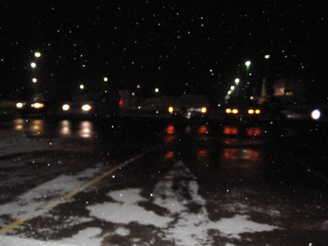 1995 Ford Thunderbird - Cars drive on a wet road at night with snow falling.