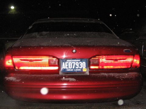 1995 Ford Thunderbird - The rear of a red sedan, possibly a 1995 Ford Thunderbird, is shown at night with snow falling.