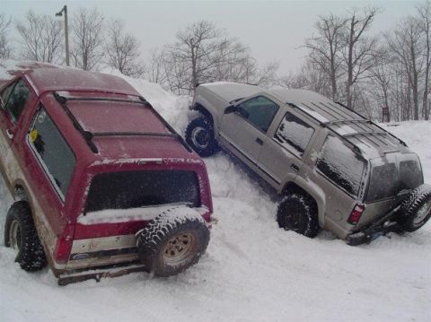 2000 Chevrolet Tahoe - A red Ford Bronco and a silver Chevrolet Tahoe are stuck in the snow, with trees in the background.