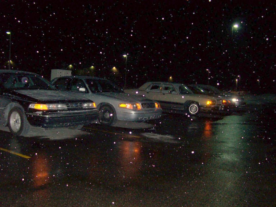 Row of sedans in a wet parking lot at night during snowfall