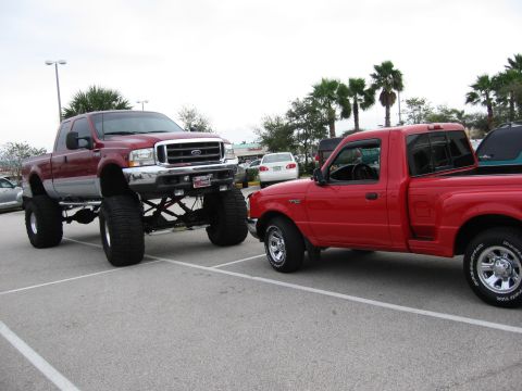 1974 Ford F-100 - Two Ford trucks are parked side-by-side in a parking lot, one is significantly lifted.