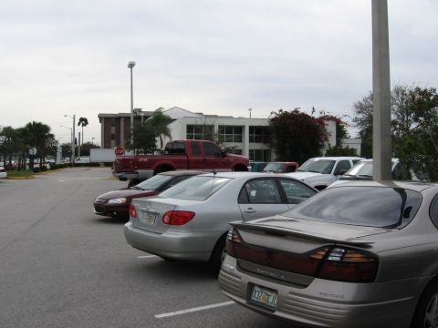 1974 Ford F-100 - A red pickup truck is parked in a lot with several other cars under an overcast sky.