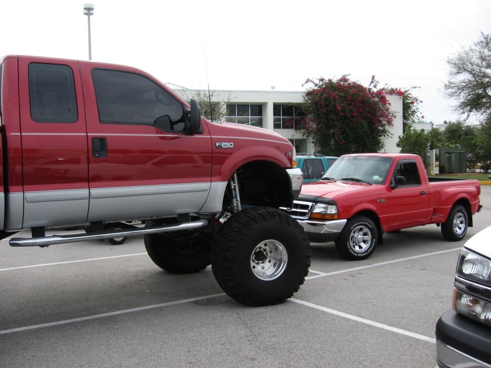 Red pickup truck with oversized tires and silver trim, parked next to a red Ford Ranger