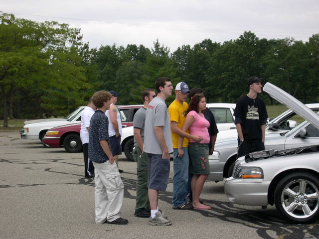 Group of people gathered around several cars, some with hoods open