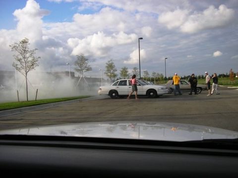 1988 Mercury Grand Marquis - A white sedan is performing a burnout, creating a large cloud of smoke, while onlookers observe.
