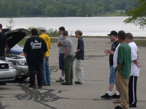 1988 Mercury Grand Marquis - Several men are gathered around a Mercury Grand Marquis with its hood open near a body of water.