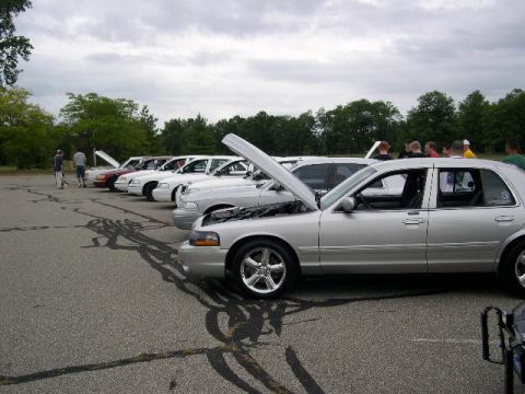 1988 Mercury Grand Marquis - A line of sedans are parked in an outdoor lot with people gathered around them.