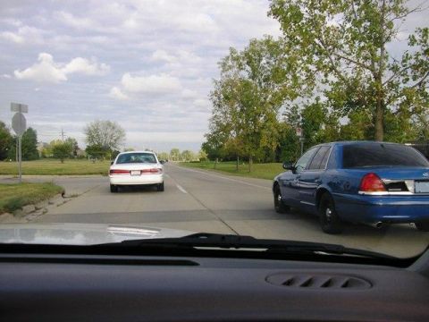 1988 Mercury Grand Marquis - Rear view of a blue police car on a road, with a white car in front.