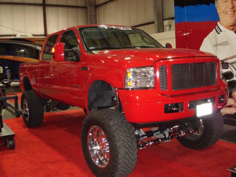 1994 Ford Bronco - This red pickup truck features a prominent chrome grille and is lifted with large off-road tires.