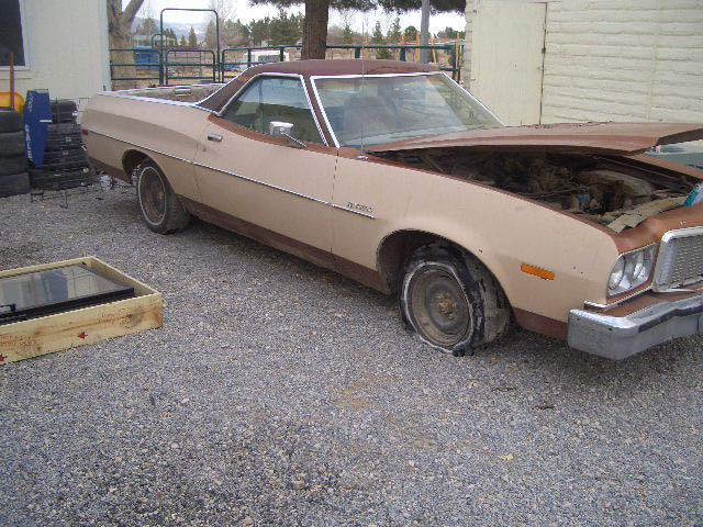 Tan and brown Ford Ranchero project with hood open and shredded front tire on gravel