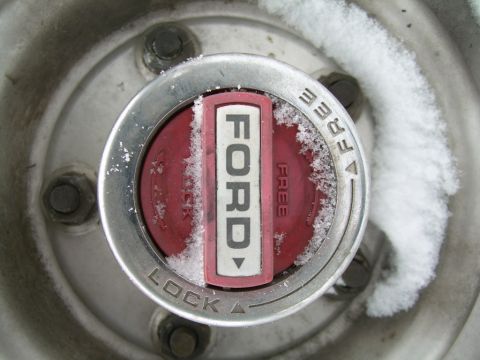 1988 Ford Bronco - A close-up of a Ford hubcap covered in snow, showing the lock and free indicators.