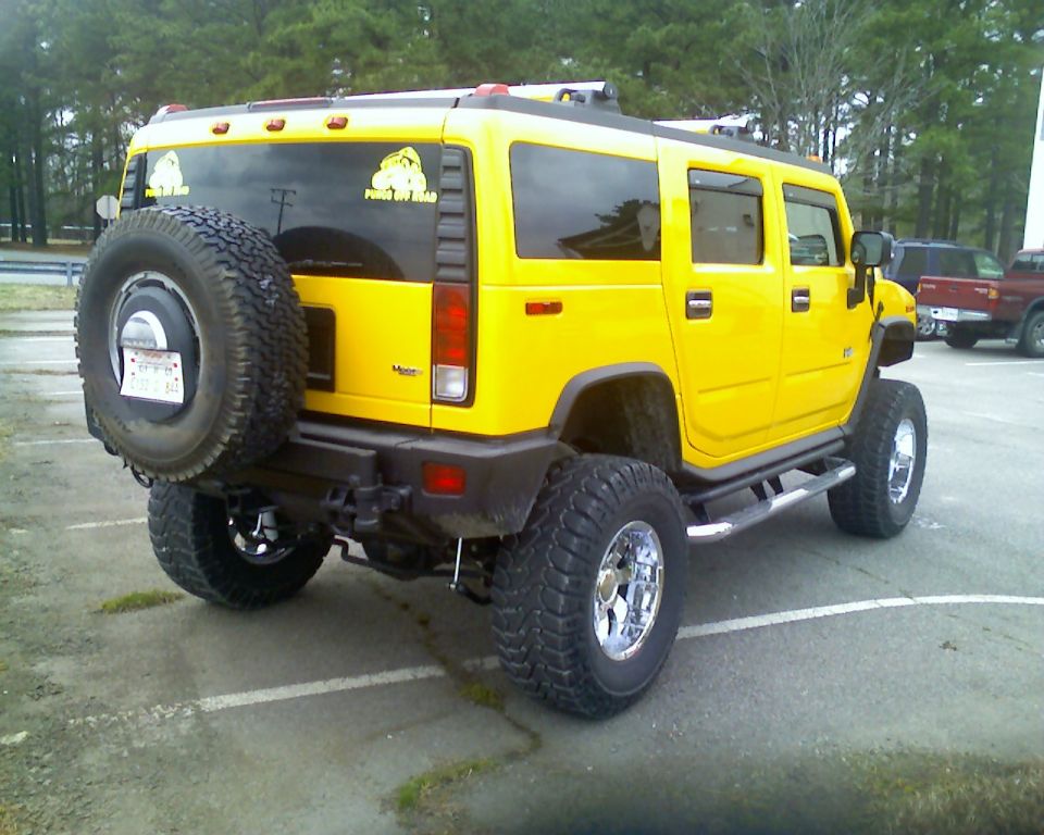 Yellow lifted Hummer H2 rear view with spare tire and chrome wheels in a parking lot