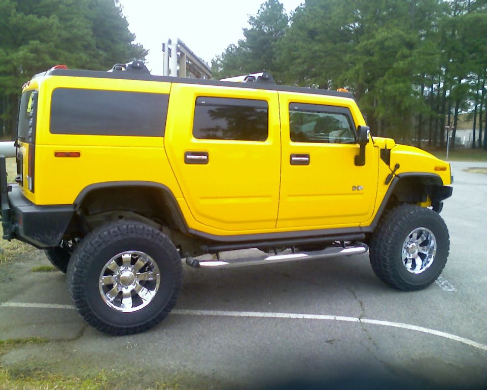 Yellow lifted Hummer H2 SUV side view on chrome wheels in a paved lot