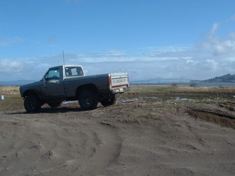 1983 Ford Ranger - This 1983 Ford Ranger pickup truck is seen from a 3/4 front angle, parked on a sandy terrain with a bridge in the background.