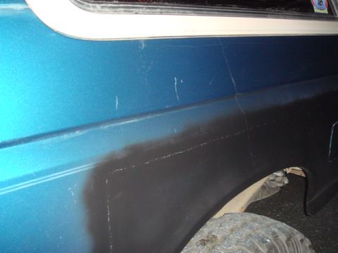 1996 Ford Bronco - Close-up of a blue vehicle's quarter panel showing areas of black primer and numerous scratches.