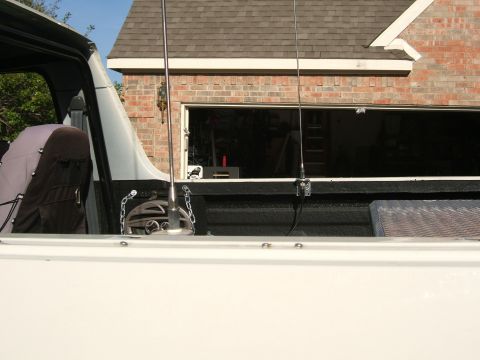 1991 Ford Bronco - View across a white truck bed with black spray-in bedliner, showing a whip CB antenna mounted to the bed rail with a spring base and tie-do…