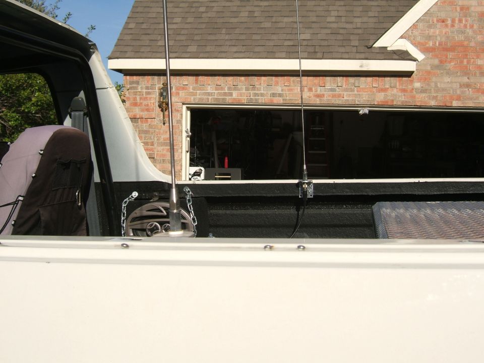 CB whip antenna mounted on bed rail of white truck with black bedliner