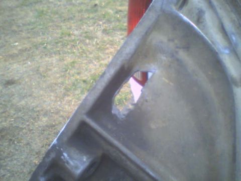 1985 Ford Bronco - This is a close-up of a metal part that has a hole in it. The background shows grass and a red object.