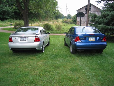 2005 Ford Focus - Two Ford Focus sedans are parked on a grassy area in front of a barn.