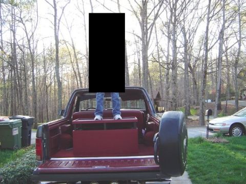 1986 Ford Bronco - Rear view of a maroon Ford Bronco with its hardtop removed and tailgate down, showing the burgundy interior and rear bench seat; a person s…