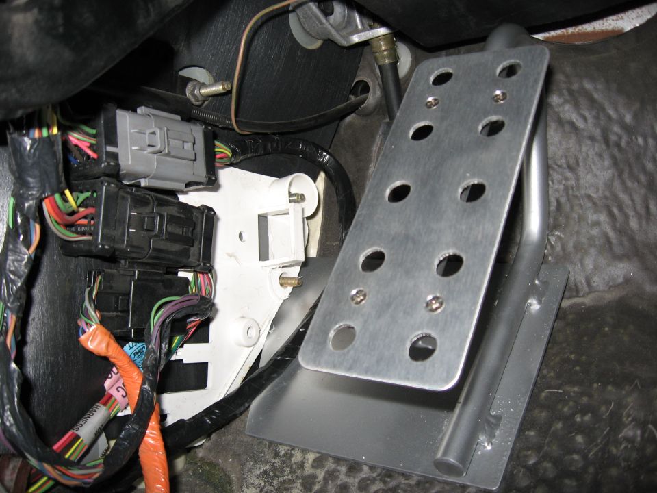 Aftermarket aluminum dead pedal bracket mounted near wiring harness connectors