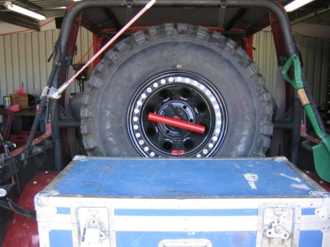 1987 Suzuki Samurai - Rear view of a 1987 Suzuki Samurai, showing the spare tire and a shovel. A blue storage case is in the foreground.