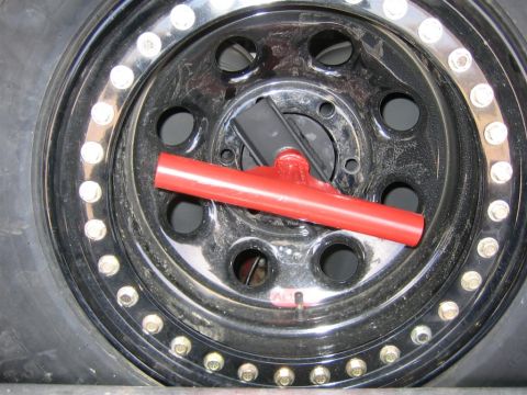 1987 Suzuki Samurai - Close-up of a spare tire with a red T-handle tire carrier and chrome lug nuts visible.