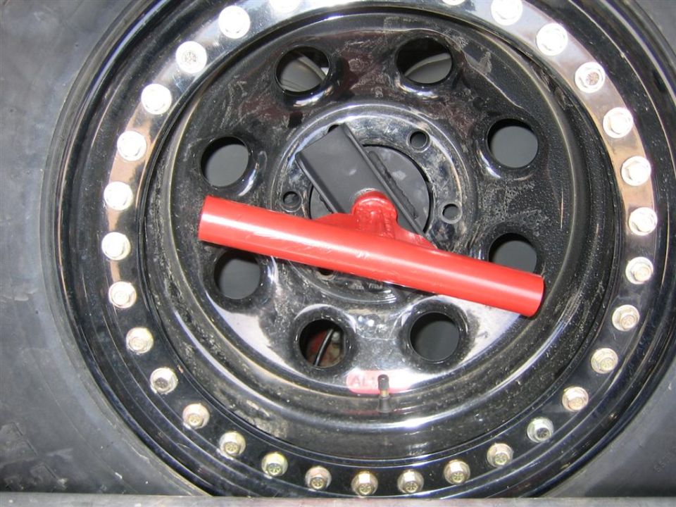 Black spare tire with red T-handle carrier and chrome lug nuts