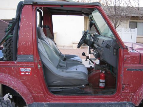 1987 Suzuki Samurai - Interior view of a red off-road vehicle, bucket seats, a steering wheel, and a fire extinguisher mounted on the floor.