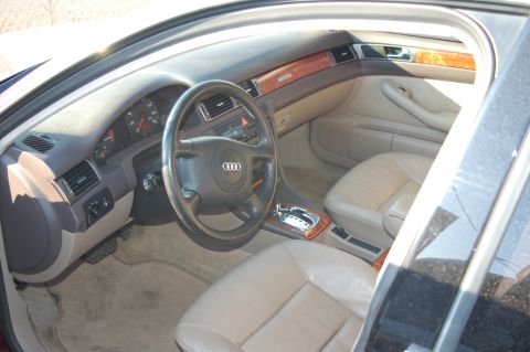 1993 Ford Bronco - The interior of an Audi A6 shows tan leather seats, wood accents, and the dashboard with the Audi rings logo on the steering wheel.
