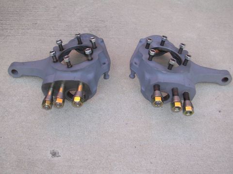 1999 Toyota Tacoma - Two gray suspension steering knuckles, each with multiple bolts and nuts, are shown on a concrete surface.