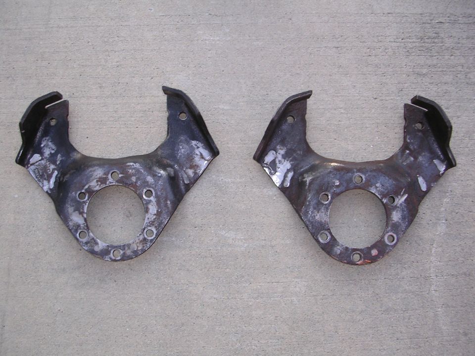 Two metal suspension knuckles with multiple bolt holes sit on concrete