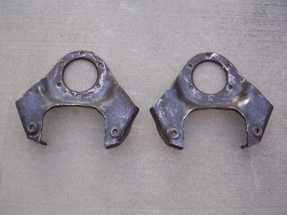 Two rusty metal suspension parts with circular openings and bolt holes, resting on a concrete surface