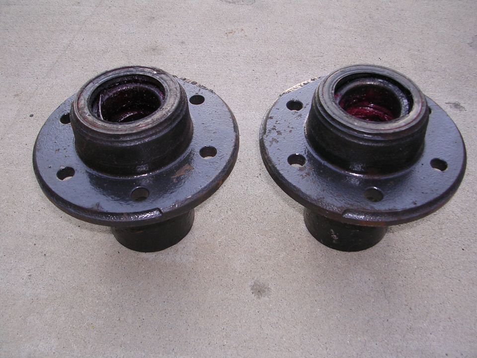 Two greased wheel hubs with four bolt holes each, resting on a concrete surface