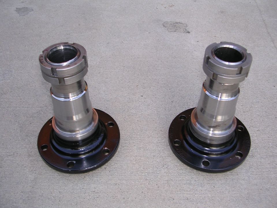 Two shiny metal axle hubs with black mounting plates sit on a concrete surface