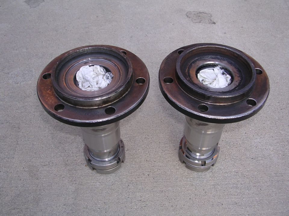 Two rusty wheel hubs with metal shafts and locking mechanisms sit on a concrete surface