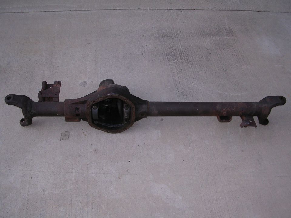 Rusty rear axle assembly with differential housing and axle tubes, resting on a concrete surface