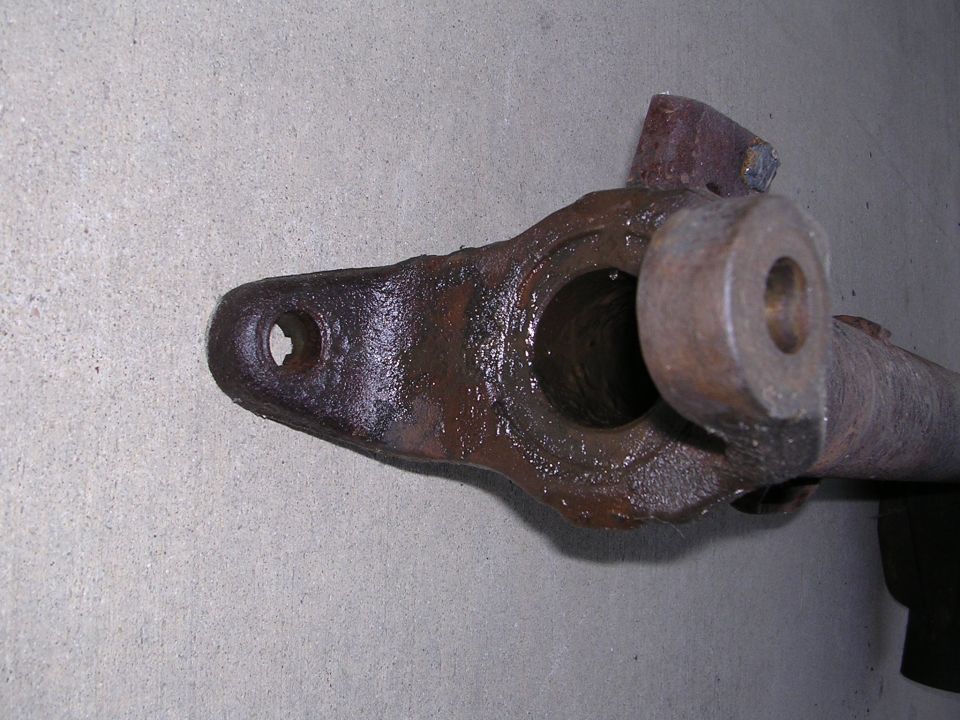 Rusted metal automotive part with holes and a cylindrical opening, against a concrete background