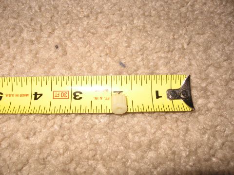 1990 Ford Bronco - A small plastic component is measured against a tape measure on a carpeted surface.
