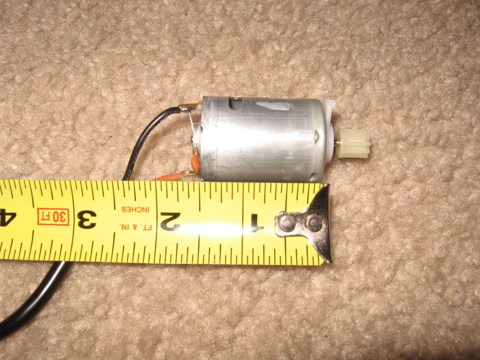 Small brushed DC motor with white pinion gear measured against a tape measure