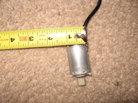 1990 Ford Bronco - A small bare-can DC electric motor with a white plastic worm gear on the output shaft and a black wire lead, laid on tan carpet next to a y…