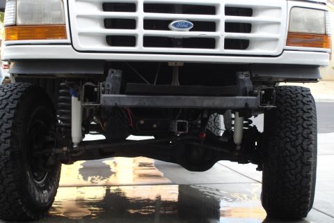 1996 Ford Bronco - The front grille and headlights of a Ford truck are visible, with the bumper removed to expose the suspension components.