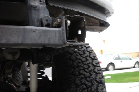 1996 Ford Bronco - Close-up view of a rear bumper mounting bracket and tire, with a white sedan visible in the background.